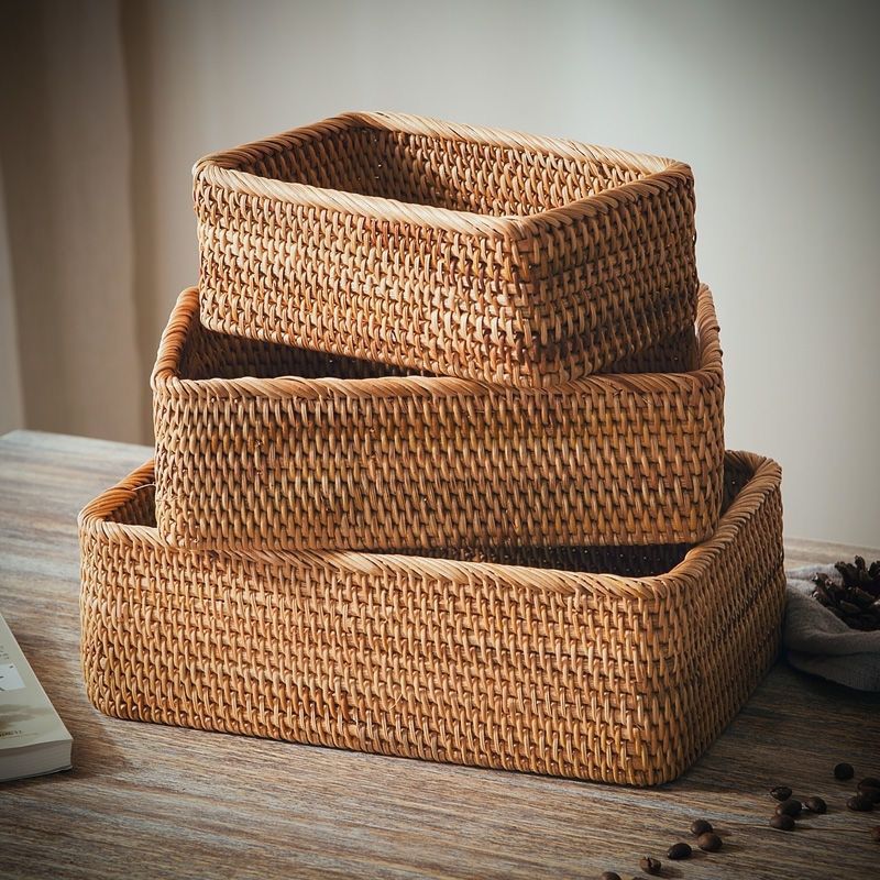 Three rectangular rattan storage baskets stacked by size on a wooden table