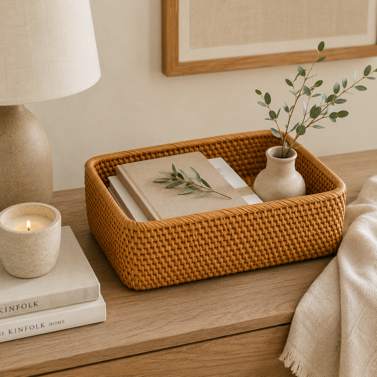 Rectangular rattan storage basket holding books and a vase on a bedside table